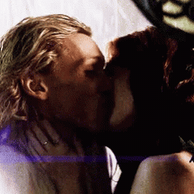 A Man And A Woman Are Kissing Each Other In A Dark Room . GIF