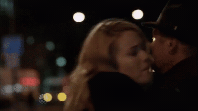 A Man And A Woman Are Kissing In A Dark Room . The Woman Is Wearing A Hat . GIF