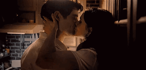 A Man And A Woman Are Kissing In A Kitchen In A Dark Room . GIF