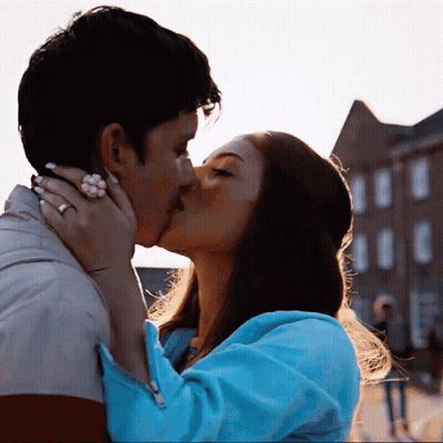 A Man And A Woman Are Kissing In Front Of A Brick Building GIF