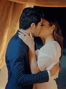 A Man And A Woman Are Kissing In Front Of A Curtain . GIF