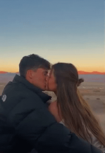 A Man And A Woman Are Kissing In Front Of A Desert Landscape . GIF