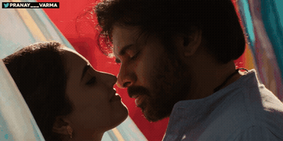 A Man And A Woman Are Kissing In Front Of A Sign That Says Pranay Varma GIF