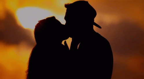 A Man And A Woman Are Kissing In Front Of A Sunset GIF