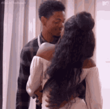 A Man And A Woman Are Kissing In Front Of A Window . The Woman Is Wearing A White Dress . GIF
