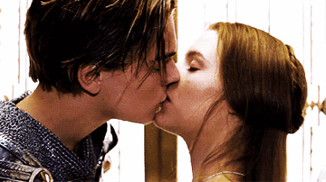 A Man And A Woman Are Kissing In Front Of A Wooden Wall GIF