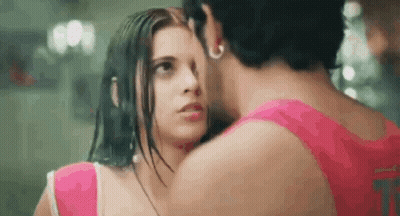 A Man And A Woman Are Kissing In The Rain And The Woman Is Wearing A Pink Top . GIF