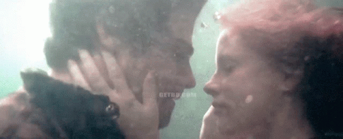 A Man And A Woman Are Kissing Underwater In The Water . GIF