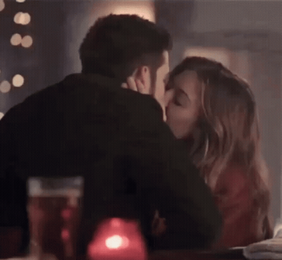 A Man And A Woman Are Kissing While Sitting At A Table In A Restaurant . GIF