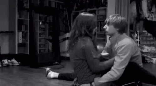 A Man And A Woman Are Kissing While Sitting On The Floor . GIF