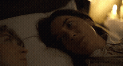 A Man And A Woman Are Laying In Bed And The Woman Is Looking At The Camera GIF