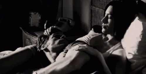 A Man And A Woman Are Laying In Bed Hugging And Kissing . GIF
