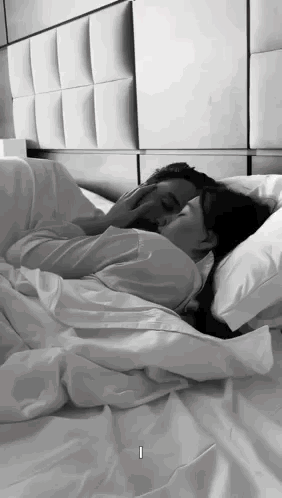 A Man And A Woman Are Laying In Bed Kissing . GIF