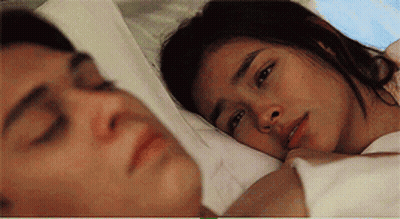 A Man And A Woman Are Laying In Bed Together And The Woman Is Looking At The Man . GIF