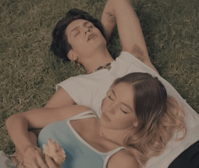 A Man And A Woman Are Laying In The Grass And The Woman Is Holding An Ice Cream Cone GIF