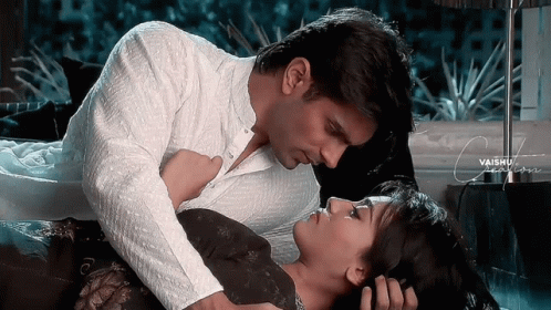 A Man And A Woman Are Laying On A Bed And The Man Is Kissing The Woman On The Forehead GIF
