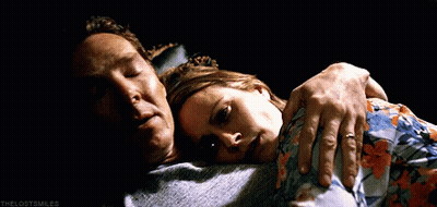 A Man And A Woman Are Laying On A Bed And The Woman Is Wearing A Floral Shirt . GIF
