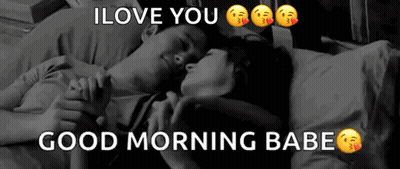 A Man And A Woman Are Laying On A Bed Holding Hands . GIF