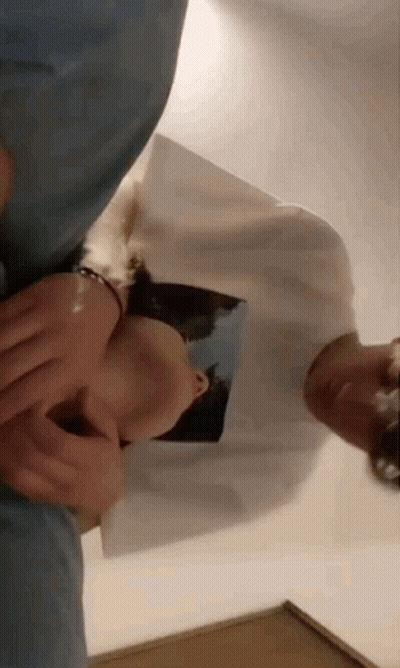 A Man And A Woman Are Laying On A Bed . The Woman Is Wearing A White Shirt With A Picture On It . GIF