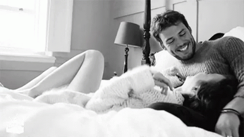 A Man And A Woman Are Laying On A Bed Together And Smiling . GIF