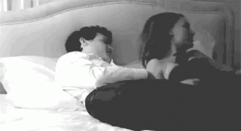 A Man And A Woman Are Laying On A Bed Together . GIF