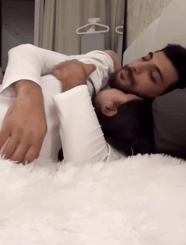 A Man And A Woman Are Laying On A Bed With Their Arms Around Each Other GIF