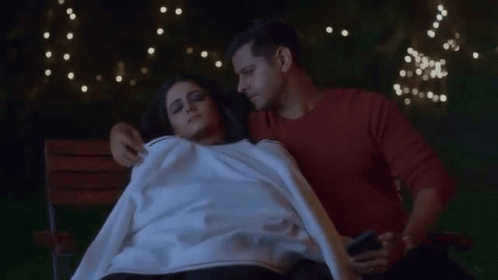 A Man And A Woman Are Laying On A Bench And The Man Is Holding A Phone GIF