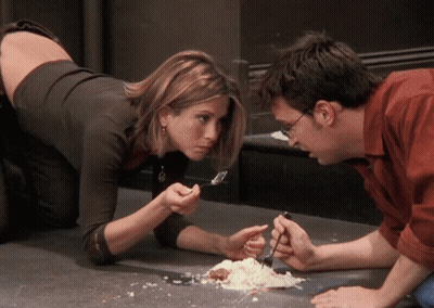 A Man And A Woman Are Looking At A Piece Of Food On The Floor GIF