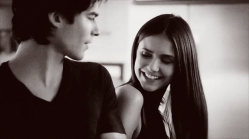 A Man And A Woman Are Looking At Each Other And Smiling . GIF