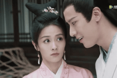 A Man And A Woman Are Looking At Each Other And The Man Is Wearing A White Shirt And The Woman Is Wearing A Pink Dress GIF