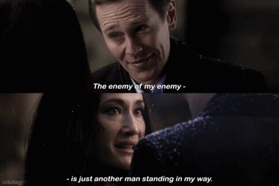 A Man And A Woman Are Looking At Each Other And The Man Says The Enemy Of My Enemy GIF