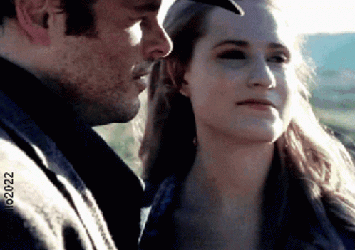 A Man And A Woman Are Looking At Each Other And The Woman Is Wearing A Hat . GIF