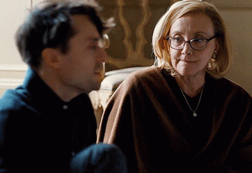 A Man And A Woman Are Looking At Each Other And The Woman Is Wearing Glasses GIF