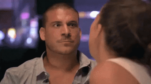 A Man And A Woman Are Looking At Each Other In A Dark Room GIF