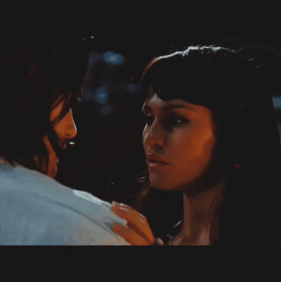 A Man And A Woman Are Looking At Each Other In A Dark Room GIF