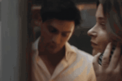 A Man And A Woman Are Looking At Each Other In A Mirror . The Man Is Covering His Ears With His Hand . GIF