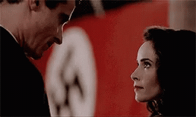 A Man And A Woman Are Looking At Each Other In Front Of A Nazi Flag . GIF
