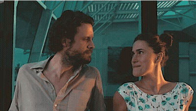 A Man And A Woman Are Looking At Each Other In Front Of A Staircase GIF