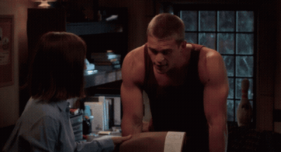 A Man And A Woman Are Looking At Each Other In Front Of A Texas Poster GIF