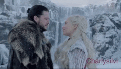 A Man And A Woman Are Looking At Each Other In Front Of A Waterfall In The Snow . GIF