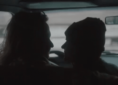 A Man And A Woman Are Looking At Each Other In The Back Seat Of A Car . GIF