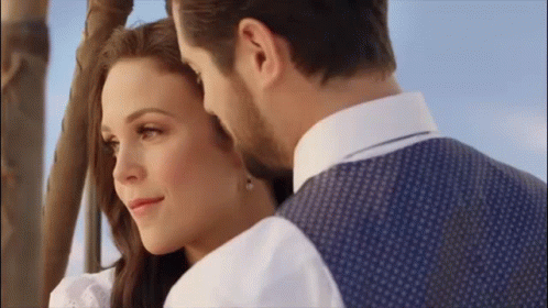 A Man And A Woman Are Looking At Each Other While Standing Next To A Hot Air Balloon . GIF
