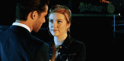 A Man And A Woman Are Looking At Each Other With A Sign In The Background That Says Mccafe GIF