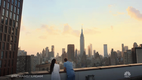 A Man And A Woman Are Looking At The City Skyline And The Empire State Building GIF