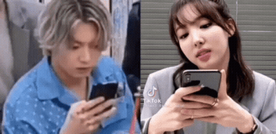 A Man And A Woman Are Looking At Their Phones . The Man Is Wearing A Blue Shirt . GIF