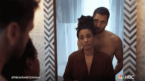 A Man And A Woman Are Looking At Themselves In A Mirror With The Hashtag #Newamsterdam On The Bottom GIF