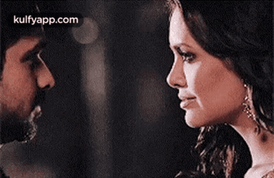 A Man And A Woman Are Looking Into Each Other 'S Eyes In A Dark Room . GIF