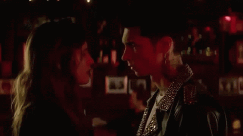 A Man And A Woman Are Looking Into Each Other 'S Eyes In A Dark Room . GIF