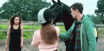 A Man And A Woman Are Petting A Horse In A Stable . GIF
