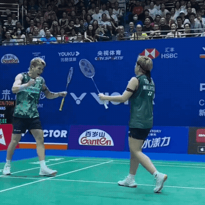 A Man And A Woman Are Playing Badminton On A Court With Advertisements For Ganten And Hsbc GIF